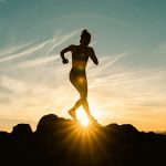 a silhouette of a woman running on a hill at sunset