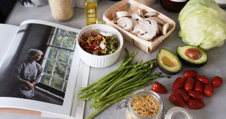 A selection of fresh vegetables and a cookbook in a kitchen setting, promoting healthy cooking.